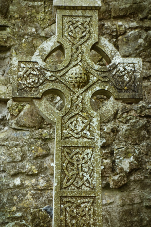 A Celtic cross against a stone wall in the graveyard of the abbey ruins in Galway, County Clare.